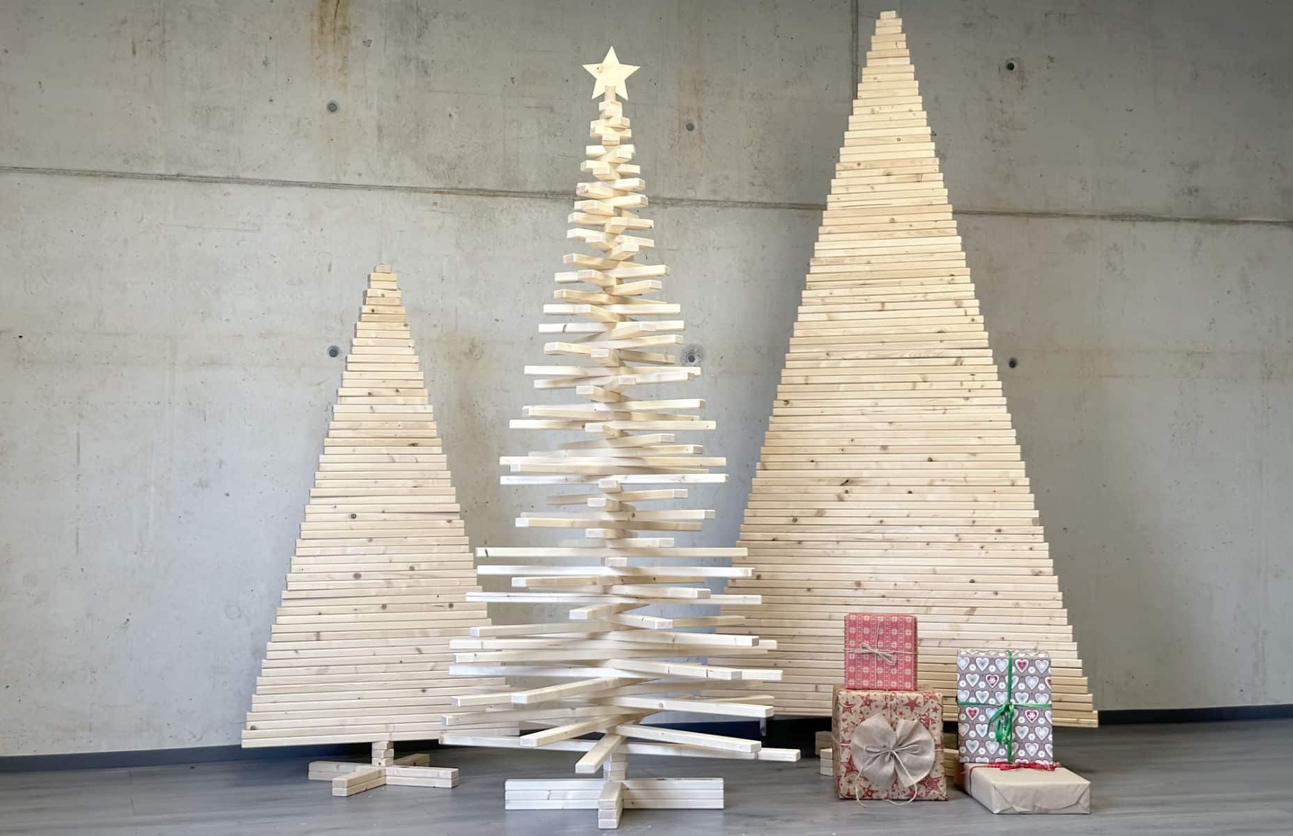 Franky Tree ist ein alternativer Weihnachtsbaum aus Holz. Auf dem Bild sind drei Holzweihnachtsbäume zu sehen in einem industriellen Setting mit Betonwänden und Geschenken vor den Bäumen